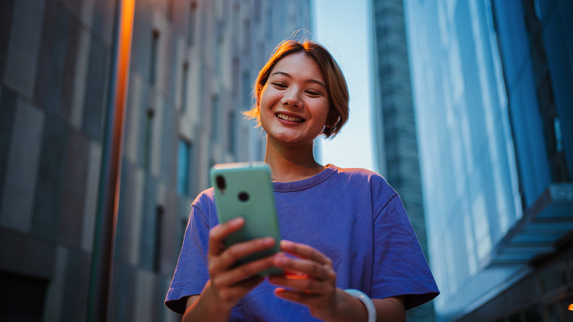 Une jeune femme souriante règle un paiement depuis son téléphone en pleine rue